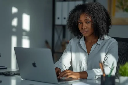 Professional Nigerian woman working on laptop at modern home office desk earning daily payments from remote jobs